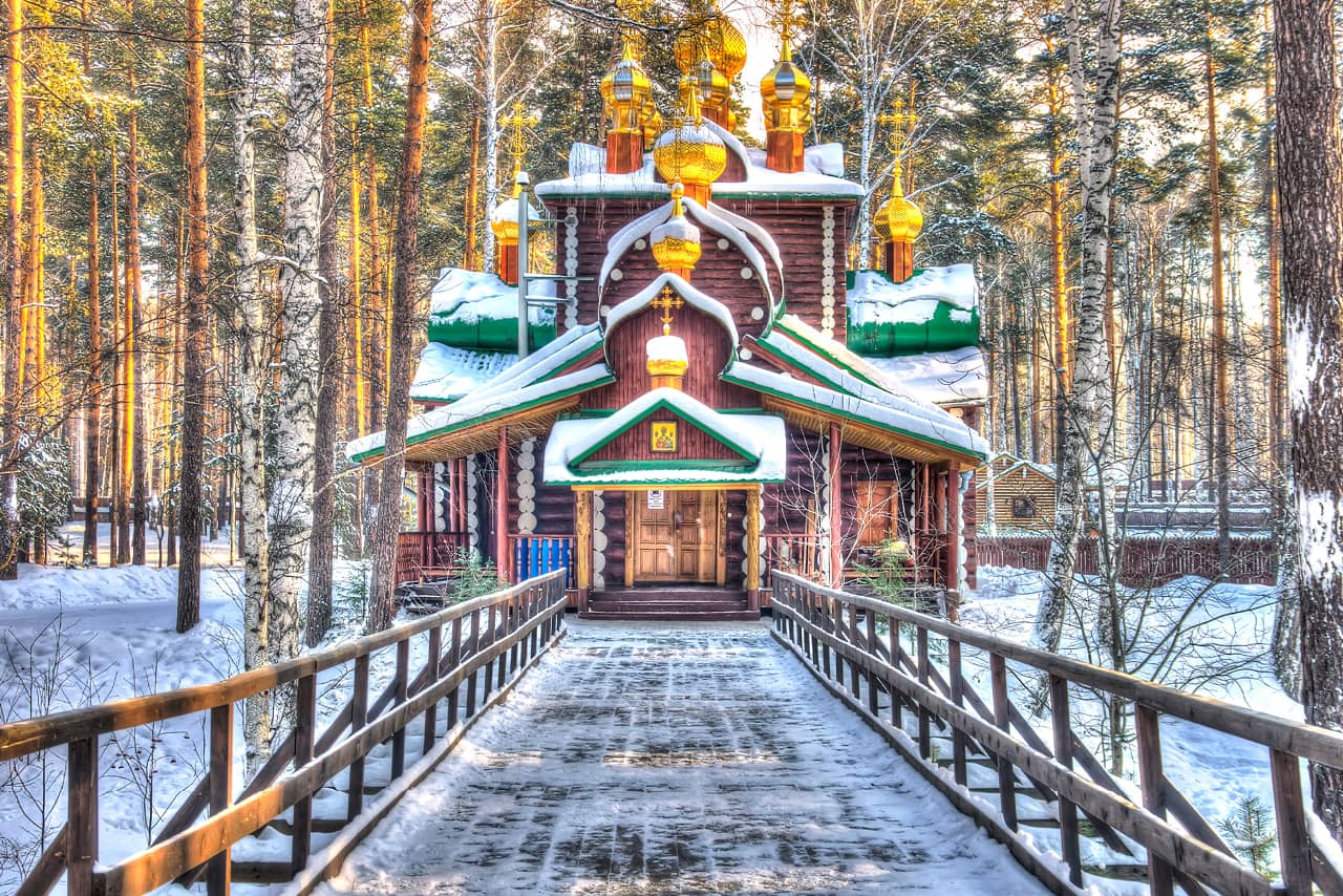 A wooden church with gilded domes in a winter forest, an icon over the entrance door