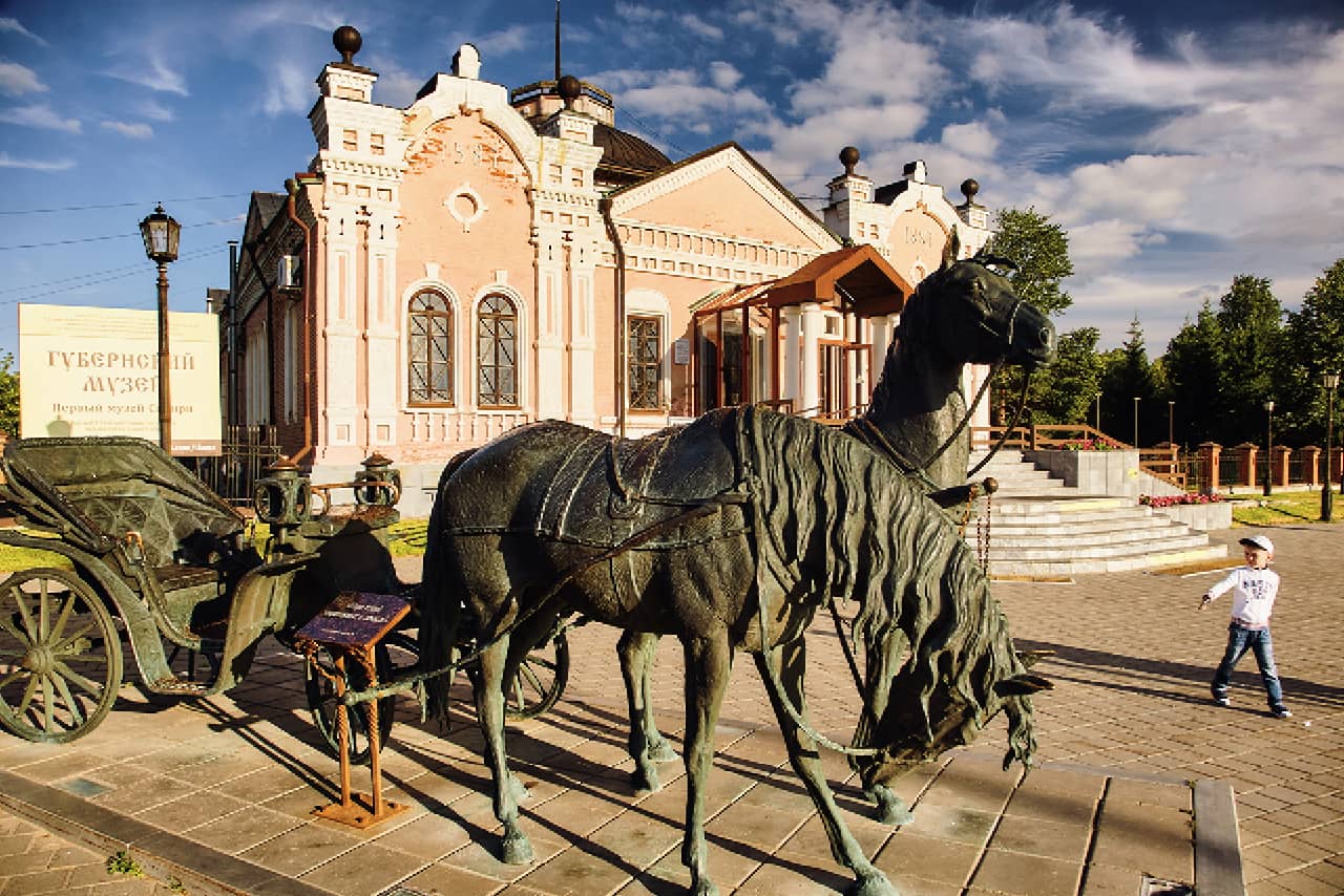A beautiful small brick white and pink building with arched wooden windows, a bronze statue of horses with a carriage