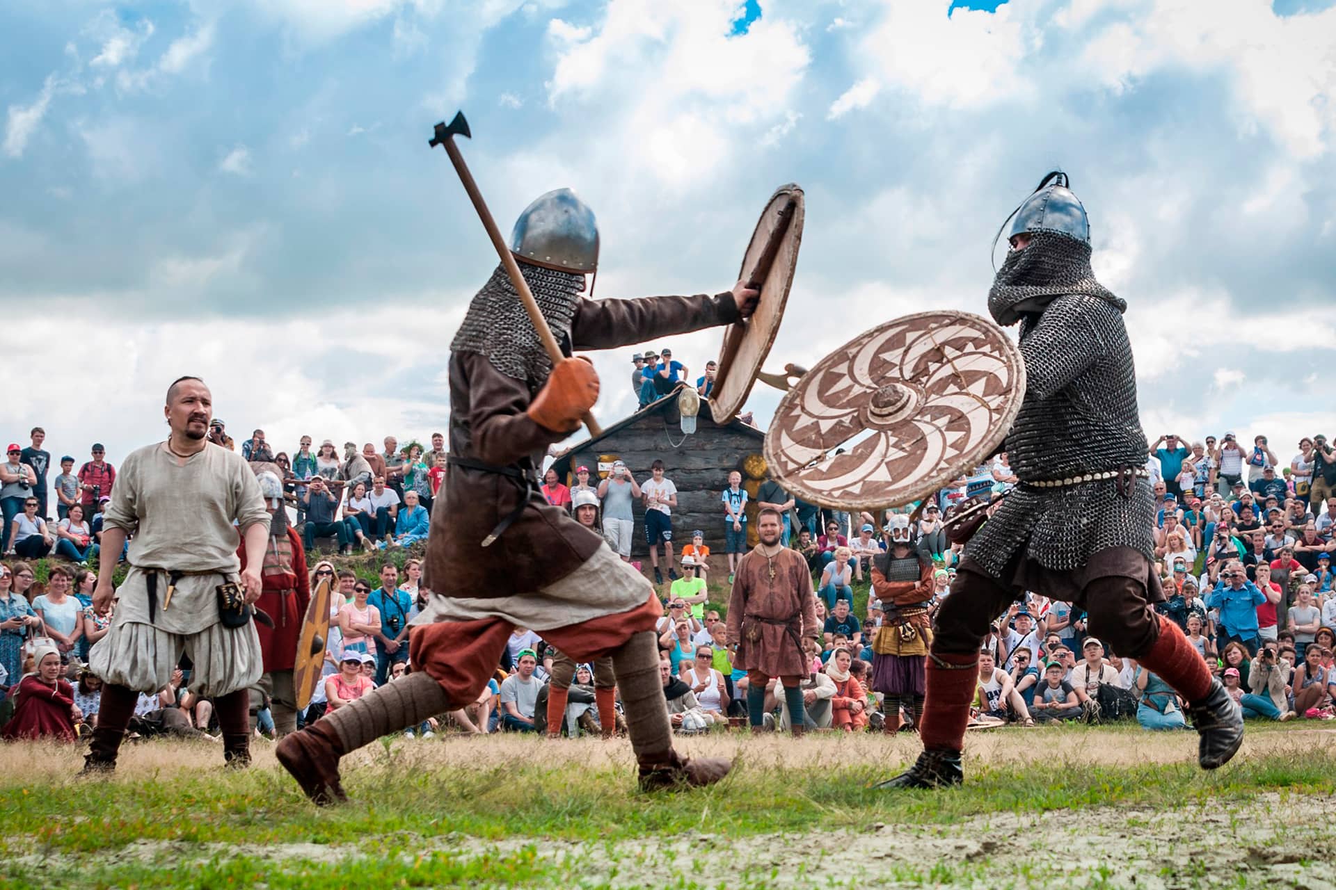 Medieval warriors wearing metal protection fighting with axes in front of audience