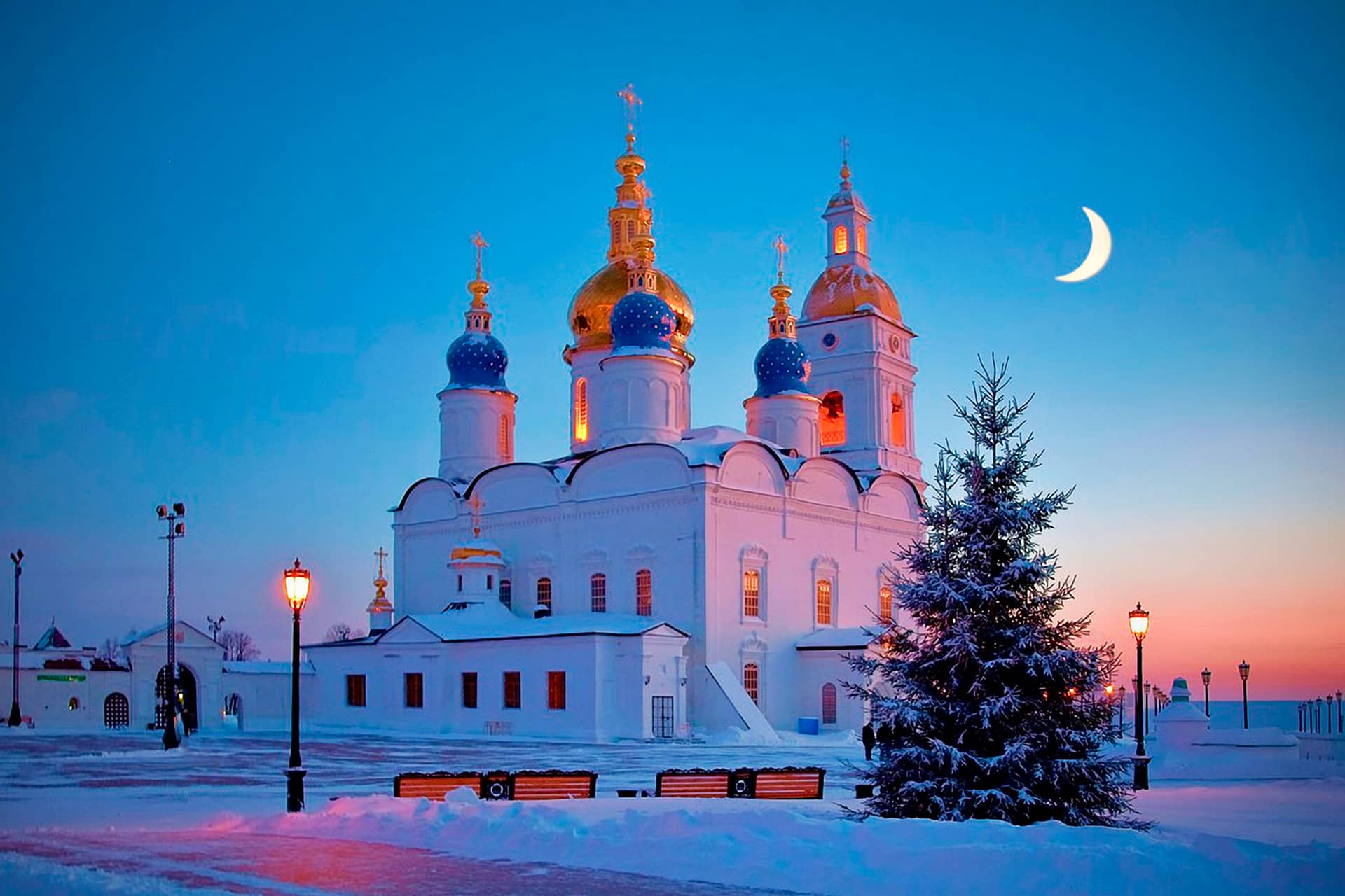 A white quadrate cathedral with one golden dome in the center and four blue smaller domes around it during the pink sunset