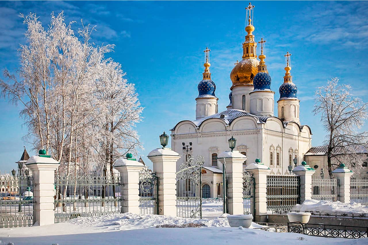 A white quadrate cathedral with one golden dome in the center and four blue smaller domes around it in winter