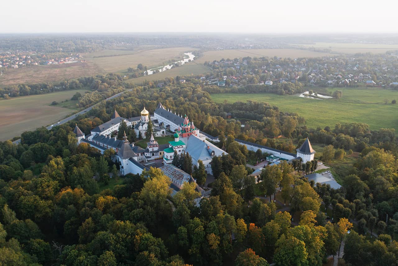 Aerial view of a well-preserved monastery hidden in the trees, territory with churches surrounded with fortress walls
