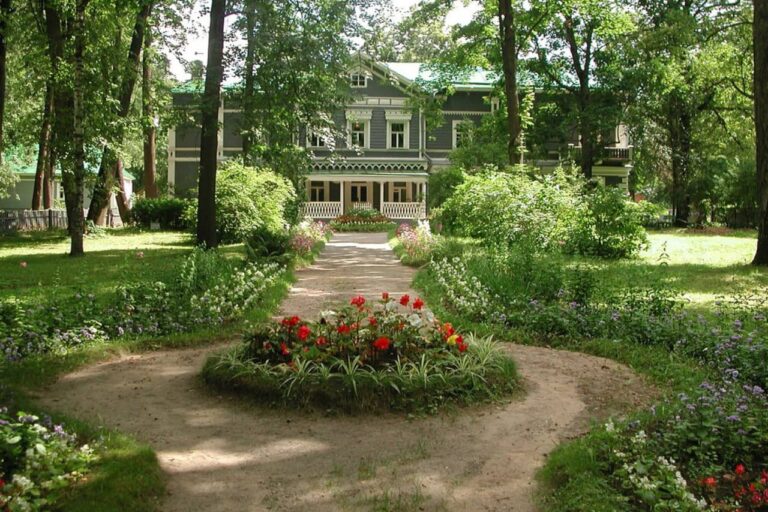 An old two-storey green wooden mansion in a park, a round flowerbed in front of the mansion
