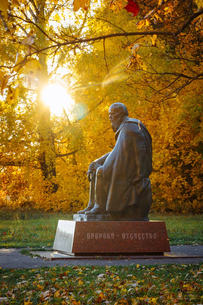 A statue of a sitting man in a park in autumn