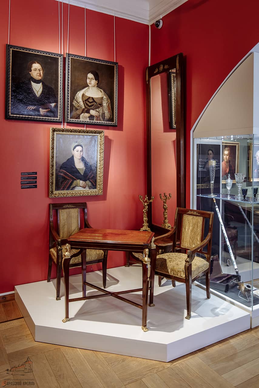A room in a museum with red walls, portraits and old furniture: table and chairs